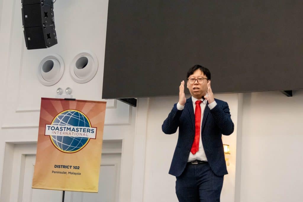 A contestant speaking on stage beside the District 102 banner
